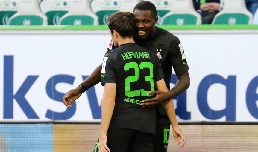 Gladbach-Stürmer Marcus Thuram bejubelt gemeinsam mit seinem Teamkollegen Jonas Hofmann einen seiner beiden Treffer beim 2:2 im Bundesliga-Duell (15. Oktober 2022) in Wolfsburg. Die beiden Spieler umarmen sich.