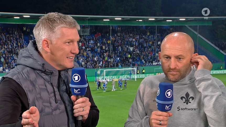 Weltmeister und ARD-Experte Bastian Schweinsteiger (l.) im Gespräch mit Darmstadt-Trainer Torsten Lieberknecht nach dem DFB-Pokal-Spiel der Lilien gegen Borussia Mönchengladbach am 18. Oktober 2022. Beide halten jeweils ein Mikrofon in der Hand.