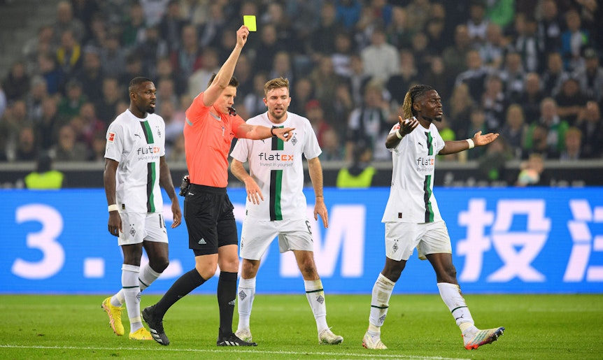 Schiedsrichter Daniel Siebert zeigt Manu Koné (r.) von Borussia Mönchengladbach die Gelbe Karte im Bundesliga-Topspiel (22. Oktober 2022) gegen Eintracht Frankfurt. Koné ist damit nicht einverstanden und gestikuliert.