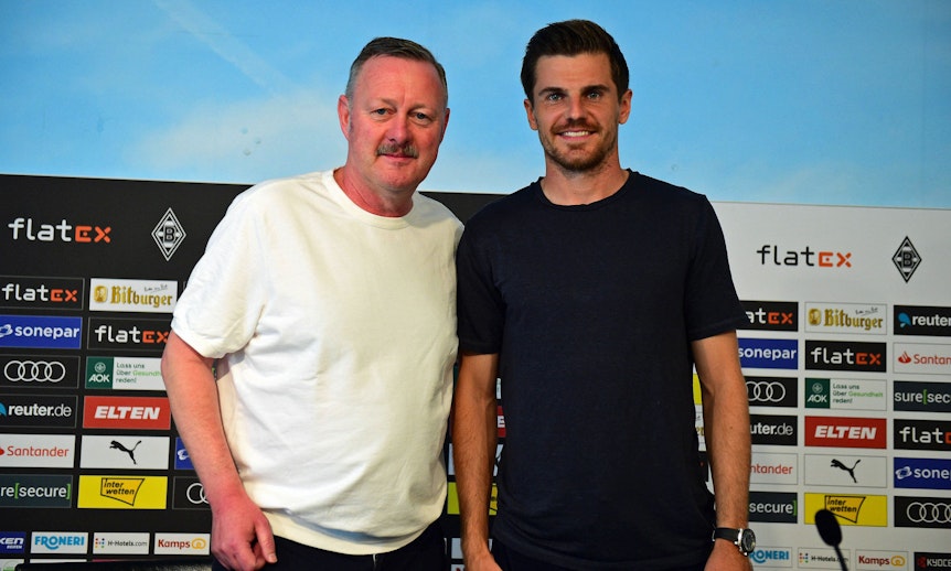 Gladbach-Manager Roland Virkus (l.) ist stolz auf seinen DFB-Nationalspieler Jonas Hofmann (r.), der am Donnerstag (10. November 2022) von Bundestrainer Hansi Flick für die WM in Katar nominiert worden ist. Auf diesem Foto sind die beiden am 9. August im Borussia-Park zu sehen. Virkus und Hofmann lächeln und schauen in die Kamera des Fotografen.