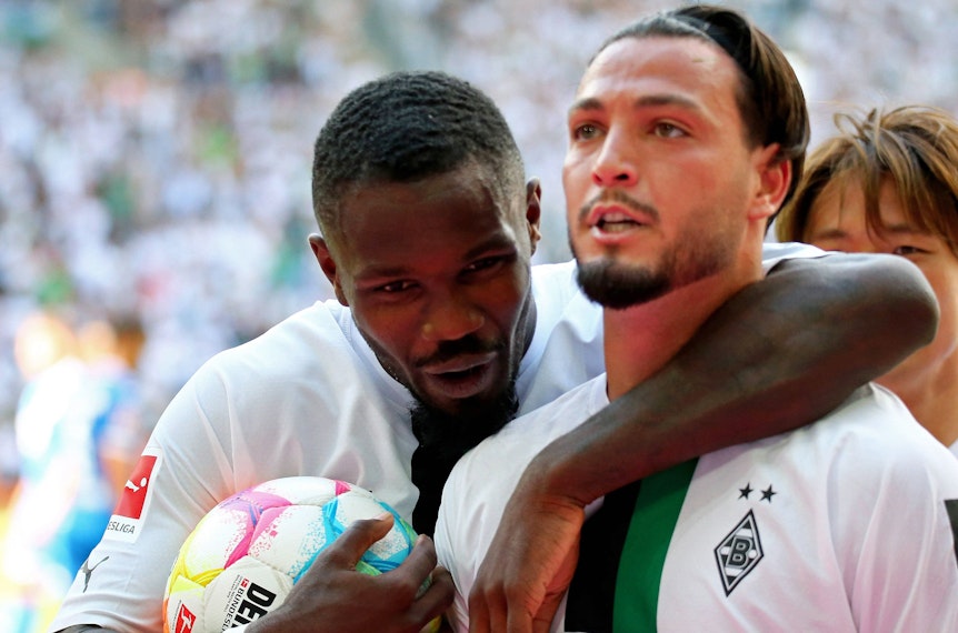 Gladbach-Profi Ramy Bensebaini (r.) bejubelt gemeinsam mit Team-Kollege Marcus Thuram (l.) einen Treffer in der Fußball-Bundesliga. Auf diesem Foto sind die beiden Borussia-Spieler am 6. August 2022 im Borussia-Park zu sehen. Thuram umarmt Bensebaini.