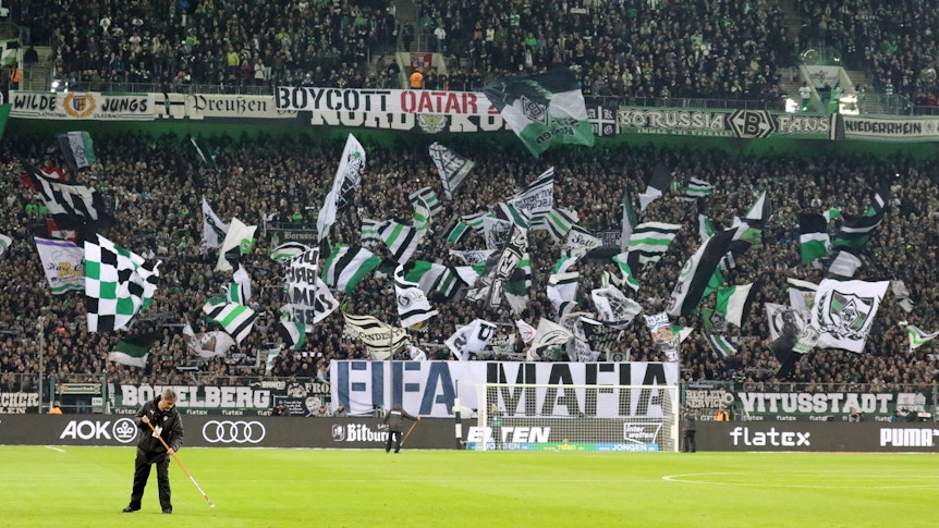 Die Fans in der Nordkurve im Borussia-Park: Dieses Foto zeigt den Anhang von Fußball-Bundesligist Borussia Mönchengladbach vor der Partie gegen Borussia Dortmund (11. November 2022). Im Vordergrund ist noch ein Greenkeeper bei der Arbeit kurz vor Anpfiff zu sehen.