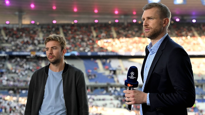 Gladbach-Profi Christoph Kramer (l.) und Per Mertesacker am 28. Mai 2022 beim Champions-League-Finale in Paris. Mertesacker hält ein Mikrofon in der rechten Hand.