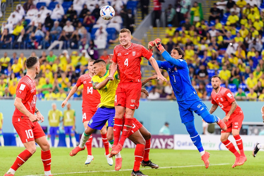 Nico Elvedi von der Schweizer Nationalmannschaft springt hoch, um einen Ball gegen Brasilien wegzuköpfen. Yann Sommer springt dem Ball mit beiden Fäusten entgegen.