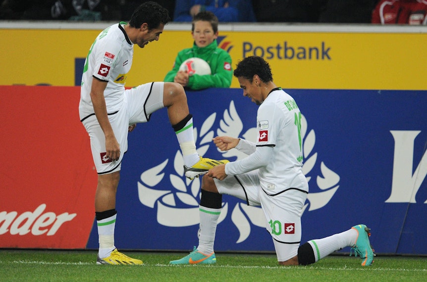 Zeige mir deinen Zauberhuf! Juan Arango (l.) und Igor de Camargo mit einer Jubelgeste am 28. November 2012 im Borussia-Park. Am Samstag (17. Dezember 2022) kehren die beiden zum Legendenspiel nach Gladbach zurück. Auf diesem Foto hat Arango seinen linken Fuß auf den Oberschenkel von de Camargo gestellt. Dieser kniet vor Arango.