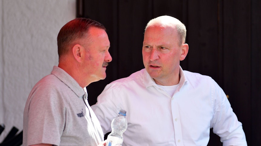Lagebesprechung unter gebürtigen Gladbachern und Borussia-Machern am bayrischen Tegernsee: Finanz-Chef Stephan Schippers (l.) im Austausch mit dem neuen Sportdirektor Roland Virkus (l.). Das Foto zeigt die beiden Borussen am 6. Juli 2022 in Rottach-Egern. Schippers spricht, Virkus hört zu, er hält in seiner rechten Hand eine Wasserflasche.