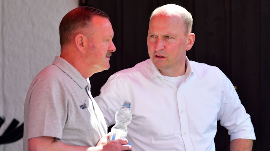 Lagebesprechung unter gebürtigen Gladbachern und Borussia-Machern am bayrischen Tegernsee: Finanz-Chef Stephan Schippers (l.) im Austausch mit dem neuen Sportdirektor Roland Virkus (l.). Das Foto zeigt die beiden Borussen am 6. Juli 2022 in Rottach-Egern. Schippers spricht, Virkus hört zu, er hält in seiner rechten Hand eine Wasserflasche.