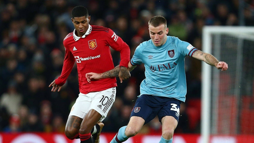 Jordan Beyer bestreitet im blauen Auswärtstrikot des FC Burnley einen Zweikampf mit Marcus Rashford, Spieler von Manchester United.