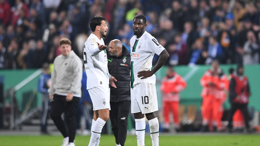 Ramy Bensebaini und Marcus Thuram stehen nach dem Spiel im DFB-Pokal bei Darmstadt 98 auf dem Rasen zusammen und reden. Bensebaini gestikuliert nach der Niederlage mit den Armen, Thuram wirkt enttäuscht.