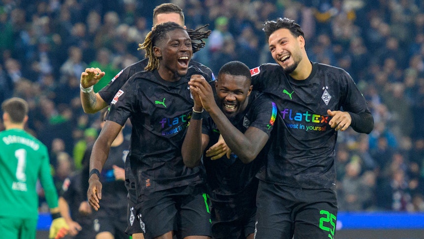 Manu Koné, Marcus Thuram und Ramy Bensebaini jubeln, lachen und liegen sich nach einem Tor im Bundesliga-Spiel gegen Borussia Dortmund am 11. November 2022 in den Armen. Die drei Gladbach-Spieler tragen schwarze Trikots und schwarze Hosen.