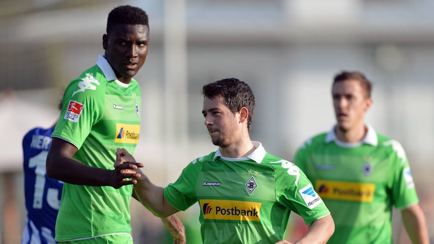 Peniel Mlapa und Amin Younes schlagen in einem Testspiel von Borussia Mönchengladbach gegen Hertha BSC am 15. Januar 2014 ein. Im Hintergrund joggt Max Kruse heran. Die Borussia-Spieler tragen ein knallgrünes Trikot.