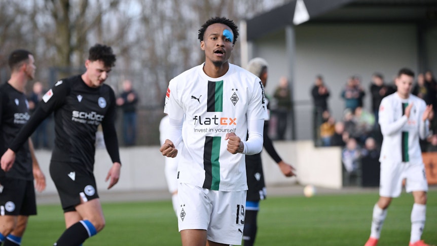 Nathan Ngoumou streckt die Arme nach oben und ballt bei seinem Jubel die Fäuste, nachdem er das 1:0 für Borussia Mönchengladbach im Testspiel gegen Arminia Bielefeld am 11. Januar 2023 erzielt hat. Ngoumou trägt das weiße Heimtrikot von Borussia und nach einer Augen-Infektion einen blauen Tape-Verband im Gesicht.