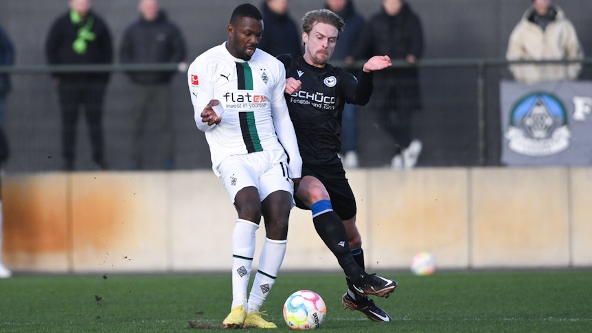 Marcus Thuram bereitet sich beim Testspiel von Borussia Mönchengladbach gegen Arminia Bielefeld am 11. Januar 2023 auf dem Fohlenplatz auf einen Schuss mit dem rechten Fuß vor, Bielefeld-Verteidiger Oliver Husing will ihn noch stoppen. Thuram trägt das weiße Borussia-Heimtrikot.