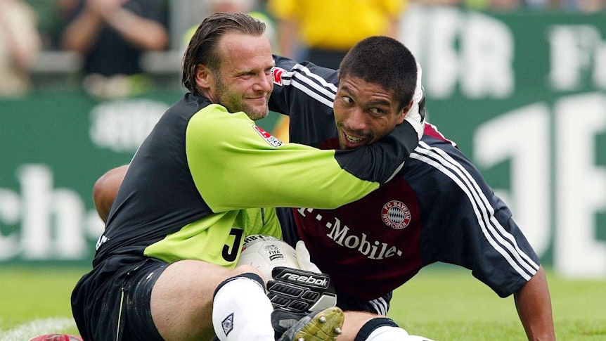Jörg Stiel (l.) umarmt Giovane Elber nach einer Parade im Spiel von Borussia Mönchengladbach gegen den FC Bayern München am 1. Spieltag der Saison 2002/2003. Beide Spieler liegen noch am Boden, berühren aber den Kopf des anderen als Fair-Play-Geste.