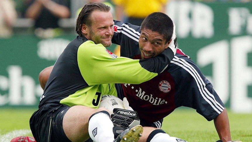 Jörg Stiel (l.) umarmt Giovane Elber nach einer Parade im Spiel von Borussia Mönchengladbach gegen den FC Bayern München am 1. Spieltag der Saison 2002/2003. Beide Spieler liegen noch am Boden, berühren aber den Kopf des anderen als Fair-Play-Geste.