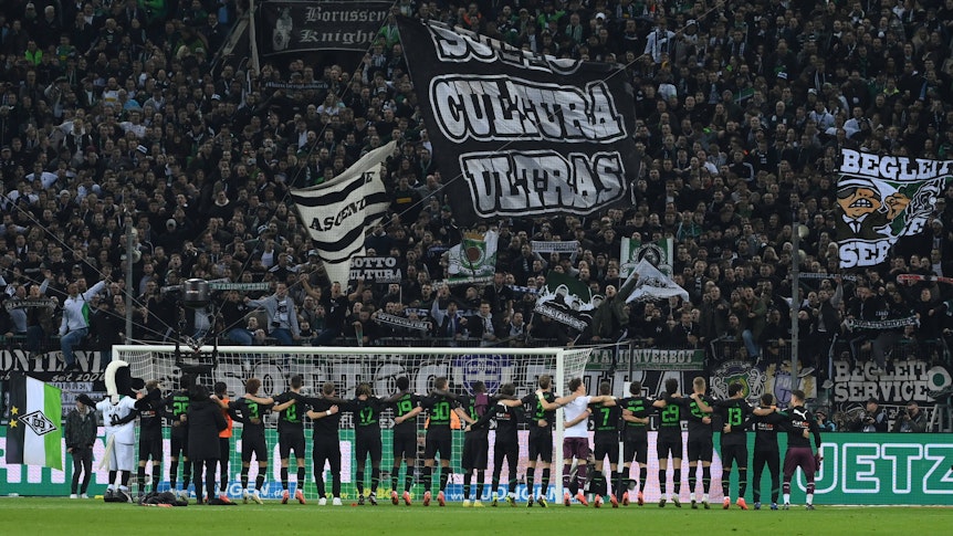Die Spieler von Borussia Mönchengladbach stehen Arm in Arm vor der Nordkurve im Borussia-Park und feiern den Bundesliga-Sieg gegen Borussia Dortmund am 11. November 2022 mit den Fans auf der Stehplatz-Tribüne.
