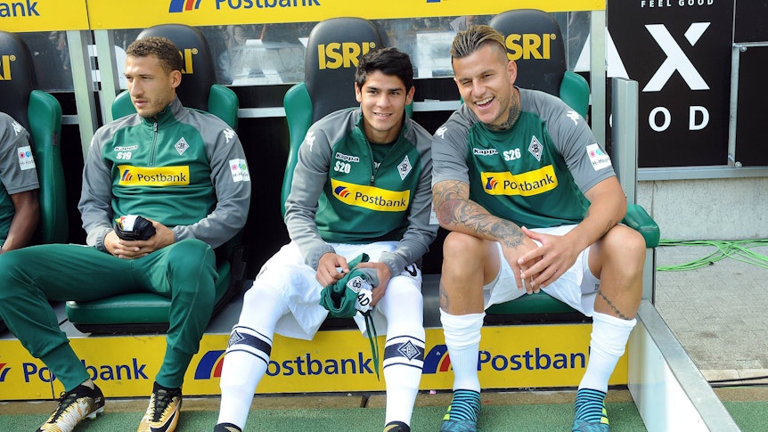 Julio Villalba (M.) sitzt am 9. September 2017 auf der Bank im Borussia-Park zwischen Fabian Johnson (l.) und Raul Bobadilla (r.). Villalba hält ein Trikot von Borussia in der Hand.