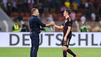 DFB-Bundestrainer Hansi Flick (l.) klatscht seinen Nationalspieler Jonas Hofmann (r.) ab. Dieses Foto zeigt die beiden am 16. November 2022 in Oman. Flick und Hofmann stehen auf dem Spielfeld.