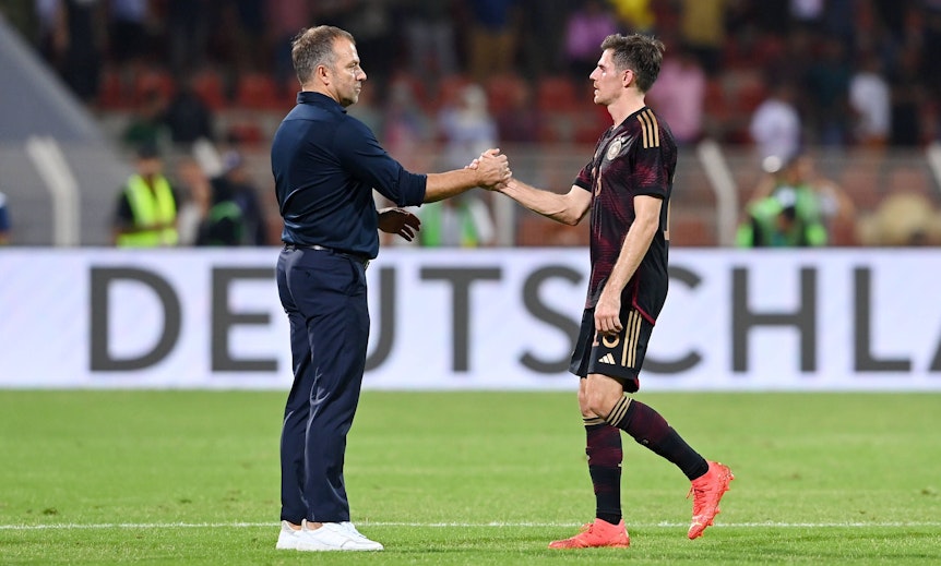 DFB-Bundestrainer Hansi Flick (l.) klatscht seinen Nationalspieler Jonas Hofmann (r.) ab. Dieses Foto zeigt die beiden am 16. November 2022 in Oman. Flick und Hofmann stehen auf dem Spielfeld.