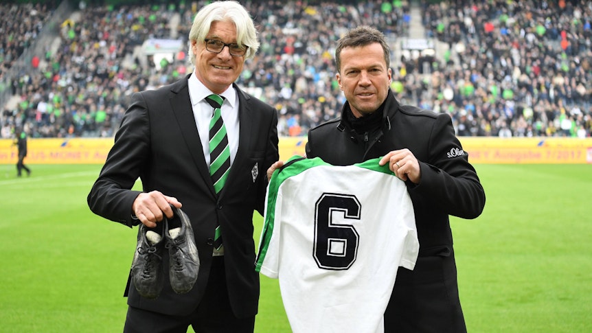 Der Mann für die Traditionspflege im Borussia-Park und der Weltmeister: Elmar Kreuels (l.) bekommt von Ex-Gladbach-Star Lothar Matthäus (r.) am 22. April 2017 dessen Original-Trikot aus alten Fohlen-Tagen samt Fußballschuhe überreicht. Beide lächeln in die Kamera. Matthäus zeigt sein Gladbach-Jersey, Kreuels hält die Schuhe in seiner rechten Hand.