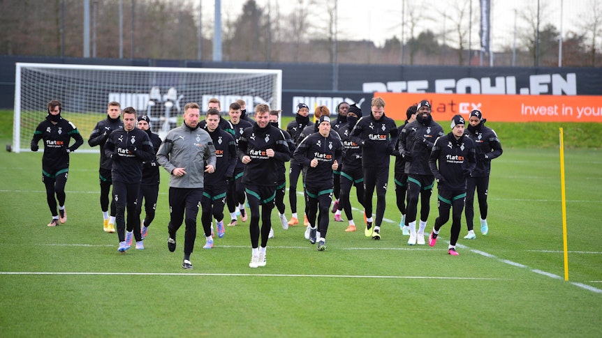 Die Spieler von Borussia Mönchengladbach laufen am 1. Februar 2023 gemeinschaftlich eine Runde auf dem Trainingsplatz-Rasen im Borussia-Park. Die Spieler tragen schwarze Gladbach-Trainingskleidung.