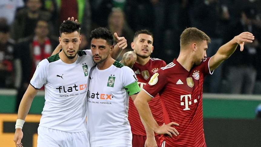 Ramy Bensebaini (l.) und Lars Stindl (2.v.l.), Spieler von Borussia Mönchengladbach, bejubeln gemeinsam einen Treffer im Spiel gegen den FC Bayern München am 27. Oktober 2021 im Borussia-Park. Stindl und Bensebaini liegen sich in den Armen. Die Bayern-Spieler Lucas Hernandez (2.v.r.) und Joshua Kimmich (r.) schauen enttäuscht drein.