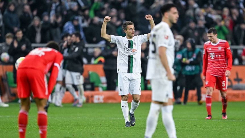 Patrick Herrmann reißt nach dem Schlusspfiff des Bundesliga-Spiels von Borussia Mönchengladbach gegen den FC Bayern München am 18. Februar 2023 die Arme nach oben. In der Nähe von Herrmann stehen die Bayern-Profis und Teamkollege Ramy Bensebaini. Herrmann trägt das weiße Gladbach-Heimtrikot.