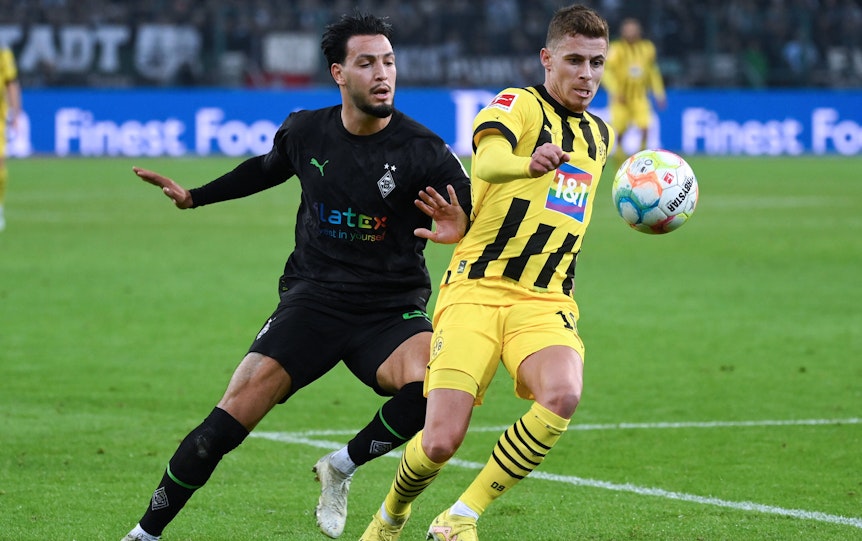 Ramy Bensebaini (l.) von Borussia Mönchengladbach im Duell mit Ex-Dortmund-Profi Thorgan Hazard (r.). Hier zu sehen im Bundesliga-Hinrunden-Match am 11. November 2022. Beide Spieler haben den Ball im Blick.