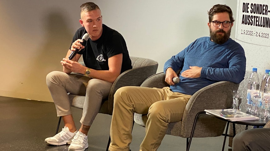 Simon Bender (l.) von der Gladbacher Ultra-Gruppierung „Sottocultura“ und der Politikwissenschaftler Jonas Gabler (r.) haben an der Diskussion (28. Februar 2023) mit Lars Stindl und Torsten Knippertz im Borussia-Park ebenfalls teilgenommen. Beide schauen zu Stindl rüber, Bender spricht in ein Mikrofon.