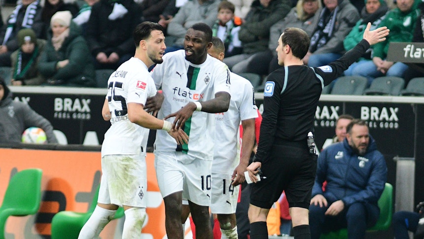 Hitzige Diskussionen im Borussia-Park! Schiedsrichter Benjamin Brand (r.) erteilt Gladbach-Profi Ramy Bensebaini (l.) einen Platzverweis (4. März 2023), Marcus Thuram (M.) ist bemüht, seinen Team-Kollegen zu beruhigen.