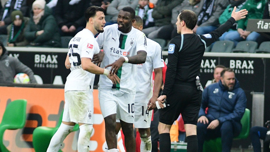 Hitzige Diskussionen im Borussia-Park! Schiedsrichter Benjamin Brand (r.) erteilt Gladbach-Profi Ramy Bensebaini (l.) einen Platzverweis (4. März 2023), Marcus Thuram (M.) ist bemüht, seinen Team-Kollegen zu beruhigen.