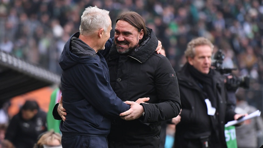 Christian Streich, Trainer vom SC Freiburg (l.), und Daniel Farke, Trainer von Borussia Mönchengladbach, begrüßen sich vor dem Bundesliga-Duell ihrer beiden Teams am 4. März 2023 im Borussia-Park. Farke und Streich umarmen sich und lächeln.