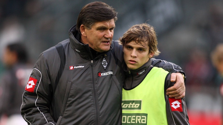 Trainer Hans Meyer (l.) spricht vor dem Bundesliga-Spiel von Borussia Mönchengladbach gegen Bayer Leverkusen am 6. Dezember 2008 mit Startelf-Debütant Tony Jantschke. Der Trainer legt beim Aufwärmen im Borussia-Park seinen Arm um den Teenager.