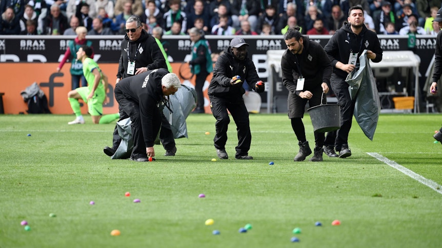 Ordner sammeln Ostereier vom Spielfeld auf, die von den Gladbach-Fans in der Nordkurve geworfen wurden.