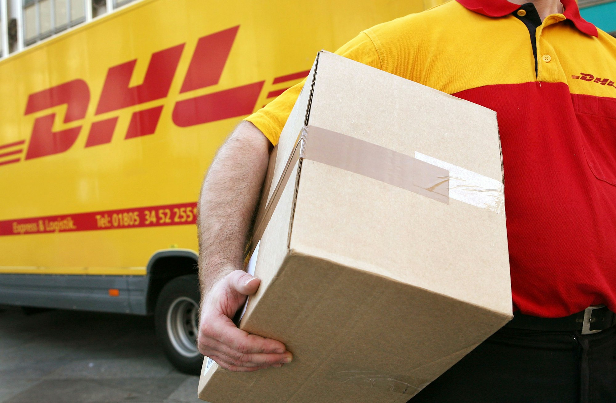 Ein Mitarbeiter des Paketdienstleisters DHL der Deutschen Post trägt ein Paket zum Kunden.