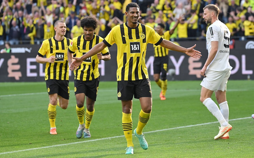 Ein Foto mit Symbolcharakter im Bundesliga-Topspiel (13. Mai 2023): Die Dortmund-Profis um Torschütze Sebastian Haller (M.) feiern eine Galavorstellung, im Hintergrund ist mit Marvin Friedrich (r.) ein enttäuschter Gladbach-Spieler zu sehen. Haller breitet die Arme aus.