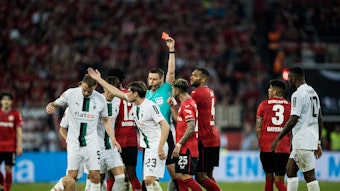 Gladbach-Star Julian Weigl liegt verletzt am Boden, Piero Hincapie von Bayer Leverkusen sieht nach seinem Foulspiel die Rote Karte (21. Mai 2023). Der Schiedsrichter hat den roten Karton in der Hand.
