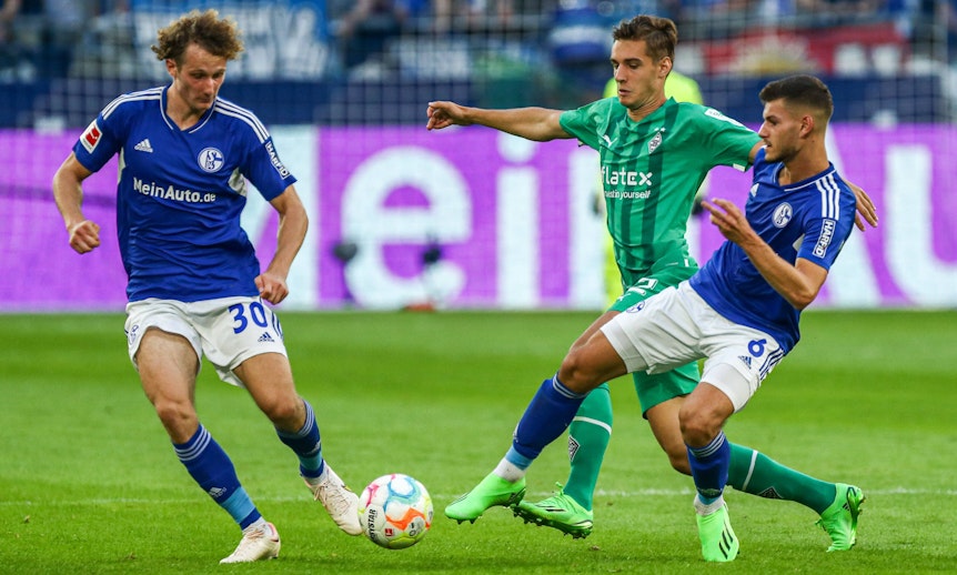 Alex Kral (l.) vom FC Schalke 04 am 13. August 2023 im Zweikampf mit Florian Neuhaus von Borussia Mönchengladbach. Daneben der Schalker Tom Krauß.