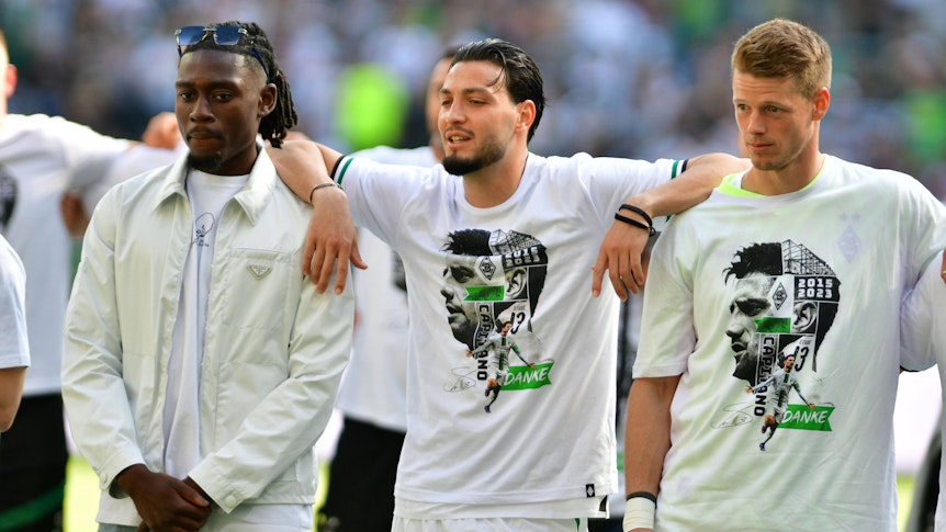 Die Gladbach-Spieler Ramy Bensebaini (M.), Manu Koné (l.) und Jonas Omlin (r.) im Borussia-Park, hier zu sehen bei der Verabschiedung von den Fohlen-Fans nach dem Bundesliga-Finale (27. Mai 2023) gegen den FC Augsburg. Die Spieler haben sich teilweise umarmt und schauen Richtung Nordkurve.