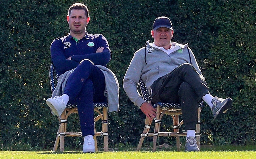 Nils Schmadtke (l.), hier zu sehen neben seinem Vater Jörg Schmadtke, als beide noch für Fußball-Bundesligist VfL Wolfsburg gearbeitet haben. Das Foto stammt vom 6. Januar 2023 und wurde während eines Trainingslagers in Portugal gemacht. Die beiden sitzen jeweils auf einem Stuhl.
