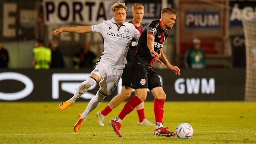 Kommt er bald zu Fußball-Bundesligist Borussia Mönchengladbach? Robin Hack (l.) von Arminia Bielefeld, hier zu sehen am 2. Juni 2023 im Relegations-Duell gegen Wehen Wiesbaden. Hack pustet im Zweikampf die Wangen auf.