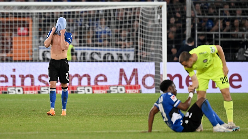Robin Hack (l.) steht nach dem Relegations-Spiel von Arminia Bielefeld gegen Wehen Wiesbaden am 6. Juni 2023 auf dem Rasen und zieht sich das Trikot über den Kopf.