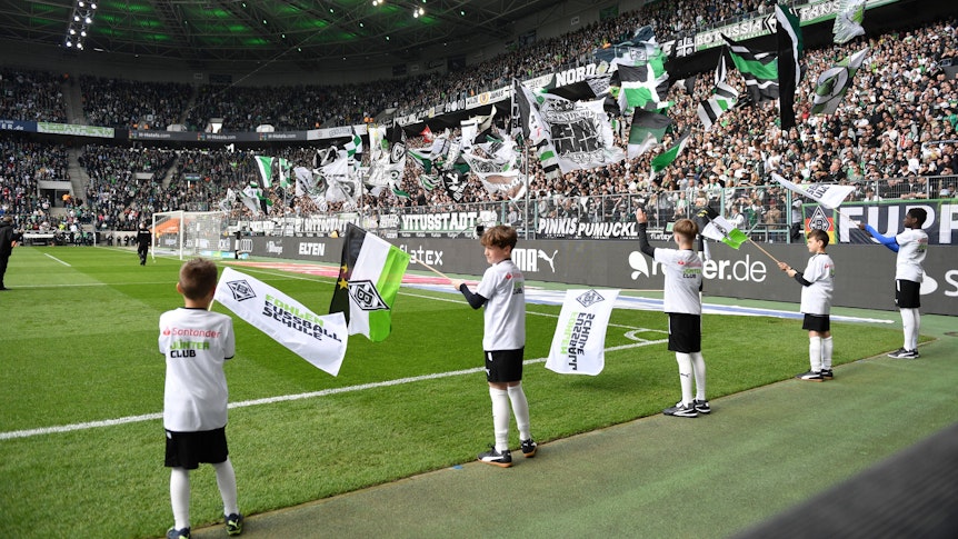 Der Borussia-Park vor einem Heimspiel von Borussia Mönchengladbach am 9. April 2023 – dazu schwenken Kinder an der Seitenauslinie Gladbach-Fahnen.