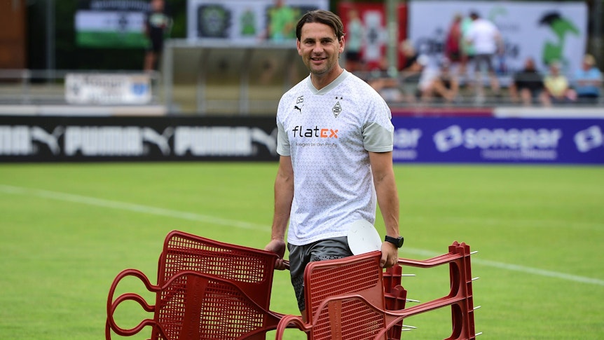 Gerardo Seoane hält am 23. Juli 2023 bei einer Einheit im Trainingslager in Rottach-Egern mehrere Spiel-Figuren in den Händen und steht auf dem Rasen am Sportplatz Birkenmoos.