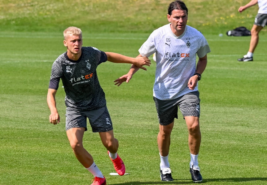 Gladbach-Profi Oscar Fraulo (l.), hier zu sehen am 11. Juli 2023 an der Seite von Cheftrainer Gerardo Seoane (l.) auf dem Trainingsgelände im Borussia-Park. Beide haben das Geschehen vor ihnen im Blick.
