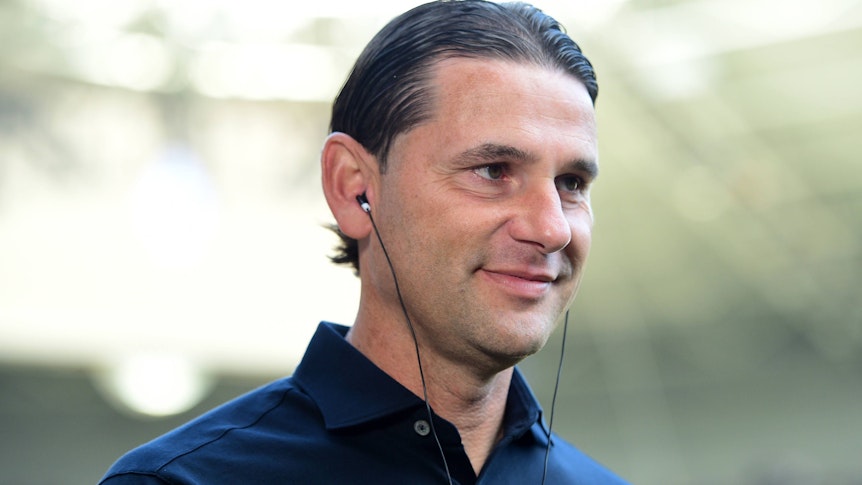 Gerardo Seoane, Trainer von Borussia Mönchengladbach, hier am 26. August 2023 im Interview vor dem Bundesliga-Spiel gegen Bayer Leverkusen, mit Kopfhörern im Ohr, seelig lächelnd.