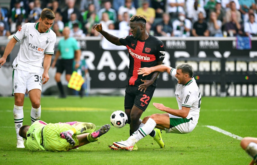 Drei Spieler von Borussia Mönchengladbach strecken sich am 26. August 2023, um Victor Boniface (Nummer 22) von Bayer Leverkusen beim Schuss zu stören.