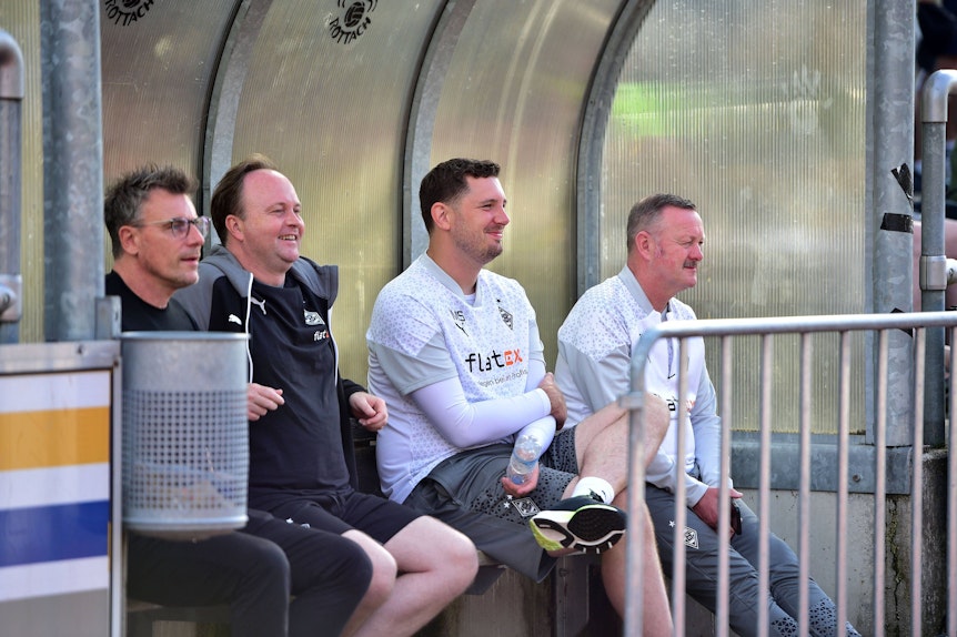 Steffen Korell, Chefscout Mario Vossen, Sportdirektor Nils Schmadtke und Roland Virkus (v.l.n.r.) sitzen im Gladbach-Trainingslager auf einer Ersatzbank.