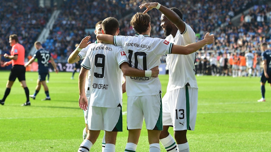 Gladbach-Spieler laufen aufeinander zu, umarmen sich und jubeln.