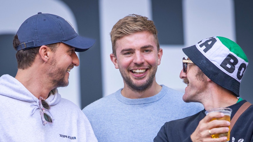 Links im Bild ist Tommi Schmitt mit einem Bier in der Hand. Neben ihm steht Christoph Kramer. Beide lachen zusammen mit einem Bekannten.